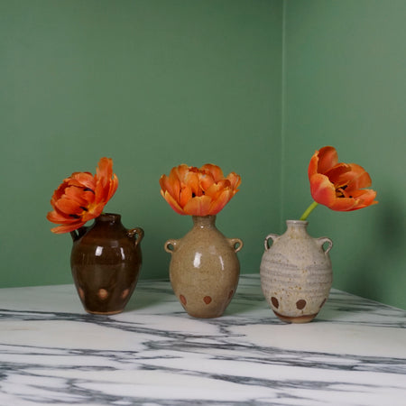 three bud vases each with a single red tulip, on a marble table with a green background. 