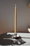 a tall beeswax candle in a candlestick holder in the bright sunshine. 