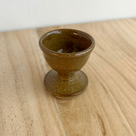 Brown ceramic egg cup on a wooden surface. Lily Pearmain Ceramics | Shop Fodder
