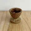Brown ceramic egg cup on a wooden surface with a white background. Lily Pearmain Ceramics | Shop Fodder