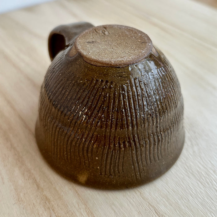 Brown ceramic cup with textured surface on a light wooden surface. Lily Pearmain Ceramics | Shop Fodder