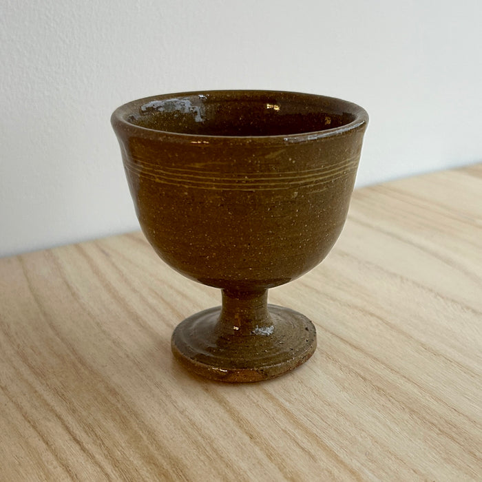 Brown ceramic goblet on a light wooden surface with a white background. Lily Pearmain Ceramics | Shop Fodder
