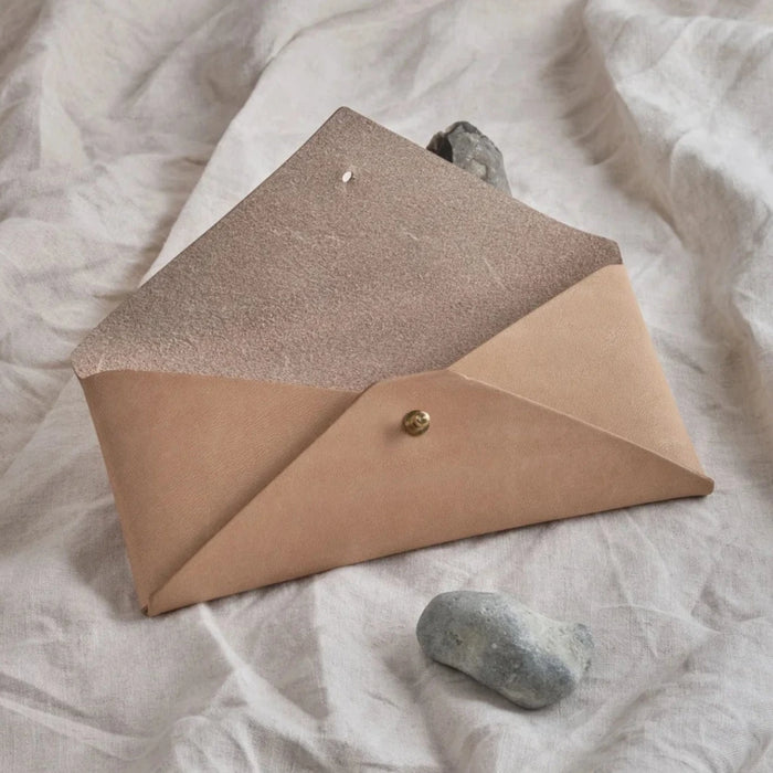 sand coloured leather envelope thats open on a cloth background. with a stone in the foreground. 