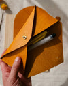Hand holding a brown leather pouch with stationery items on a neutral background