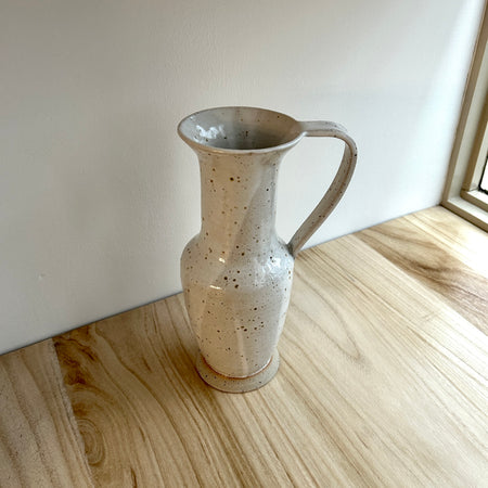 Speckled ceramic pitcher on a wooden surface with a neutral background. Mae Ceramics | Shop Fodder
