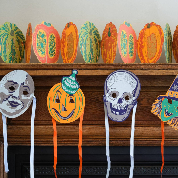 Halloween-themed masks on a wooden surface with pumpkins in the background. Masks | East End Press | Shop Fodder