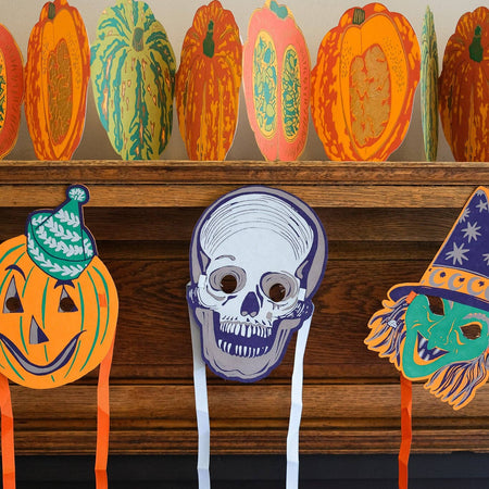 Halloween-themed masks and pumpkins on a fireplace mantle. East End Press | Shop Fodder