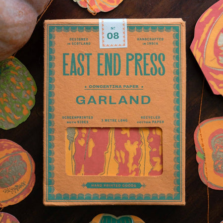 Box of East End Press Garland paper with decorative cut-out shapes on a wooden surface. Pumpkin Handprinted Garland | East End Press | Shop Fodder