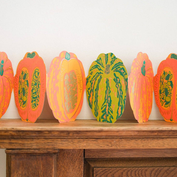 Decorative paper pumpkins on a wooden surface against a white wall. Pumpkin Handprinted Garland | East End Press | Shop Fodder