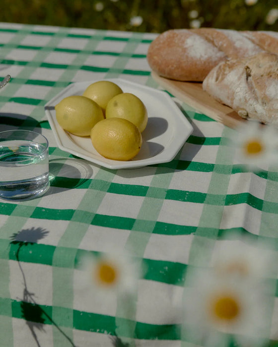 Lemons on a white plate with bread and water glass on a green checkered tablecloth