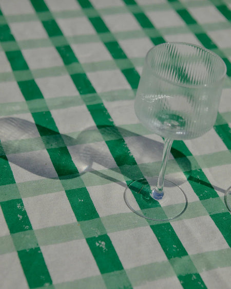 A clear ribbed glass wine glass on a green and white checkered tablecloth, casting a long shadow.