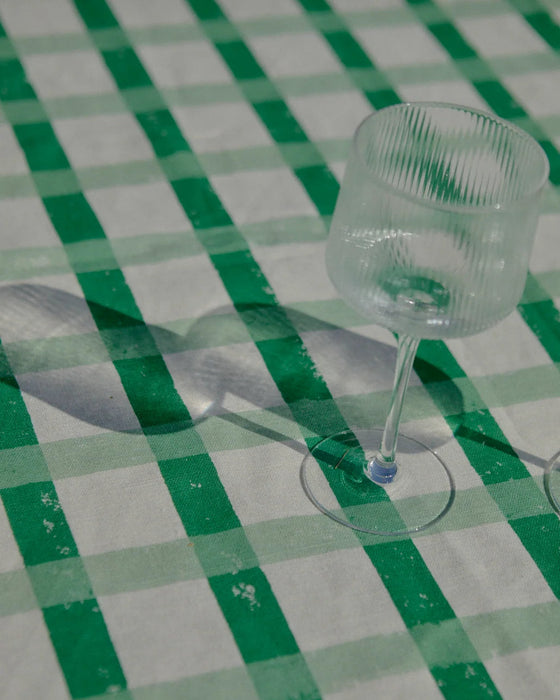 A clear ribbed glass wine glass on a green and white checkered tablecloth, casting a long shadow.