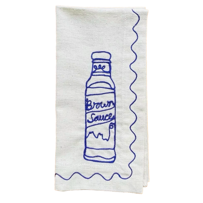 White towel with blue embroidered design of a bottle labeled 'Brown Sauce' on a white background. Embroidered Linen Napkins | See & Quin | Shop Fodder