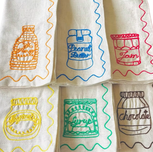 Set of embroidered napkins with colorful illustrations of food items on a white background. Embroidered Linen Napkins | See & Quin | Shop Fodder