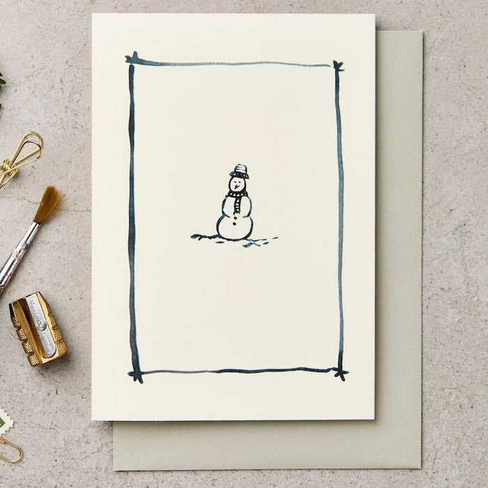 Greeting card with a snowman illustration on a textured surface with stationery items.