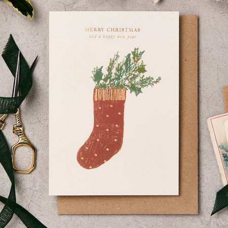 Christmas card with a red stocking illustration and 'Merry Christmas and a happy new year' text, surrounded by decorative items on a textured surface.