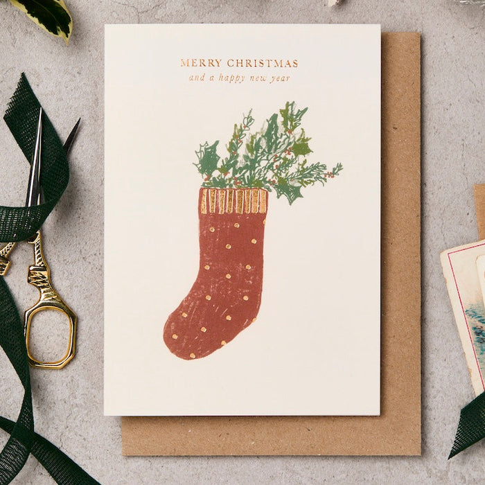 Christmas card with a red stocking illustration and 'Merry Christmas and a happy new year' text, surrounded by decorative items on a textured surface.