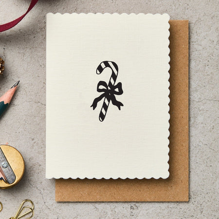 Greeting card with candy cane design, pen, and decorative items on a textured surface