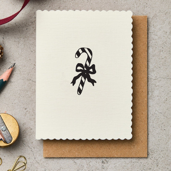 Greeting card with candy cane design, pen, and decorative items on a textured surface