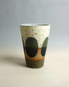 Speckled ceramic cup with green and orange design on a gradient background. Sophie Alda | Shop Fodder