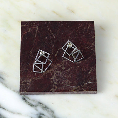 Pair of geometric silver earrings on a maroon marble surface | Scarlett French | Shop Fodder