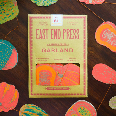 Pack of East End Press Garland paper on a wooden surface with decorative paper cutouts. Squash Autumn Handprinted Garland | East End Press | Shop Fodder