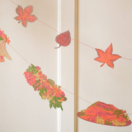 Decorative string with autumn-themed items including leaves and flowers on a light background. Thanksgiving Handprinted Garland | East End Press | Shop Fodder