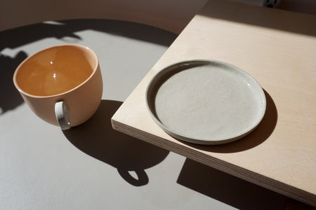a grey porcelain saucer sitting on a shelf with a peach ceramic mug next to it. 