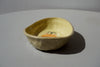 a side view of a soap dish by beci callow that looks like an avocado cut in half with a face painted on to the bottom. 