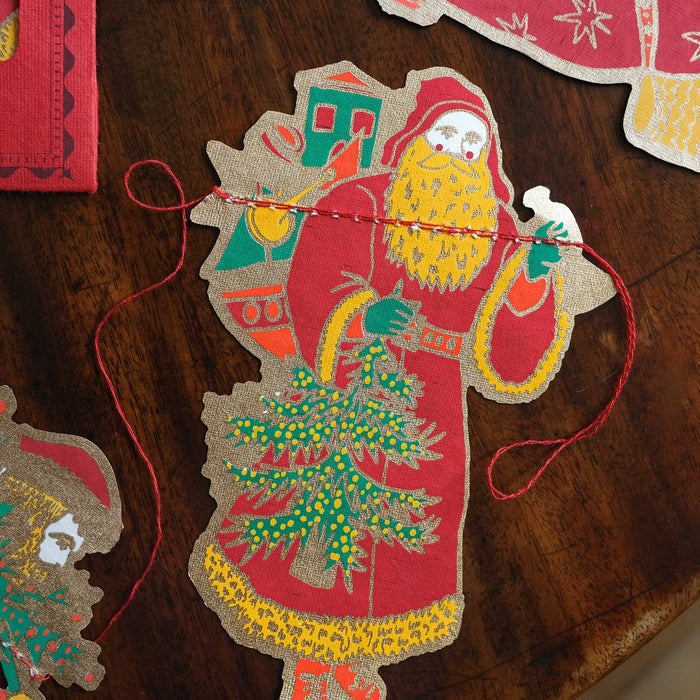 Decorative paper cutout of Santa Claus with a Christmas tree on a wooden surface. East End Press | Shop Fodder
