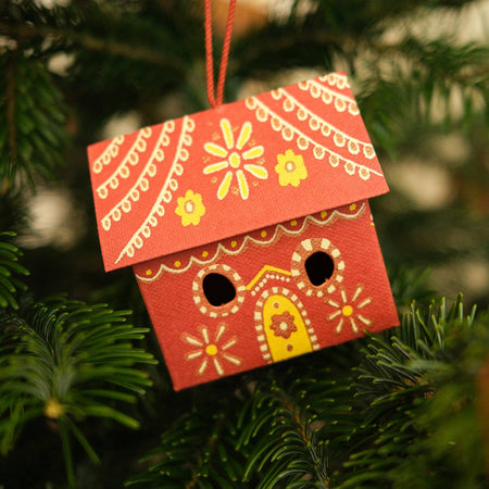 Decorative red birdhouse ornament hanging on a Christmas tree. East End Press | Shop Fodder