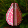 Decorative pink teardrop ornament with intricate patterns hanging against a green foliage background. | East End Press | Shop Fodder