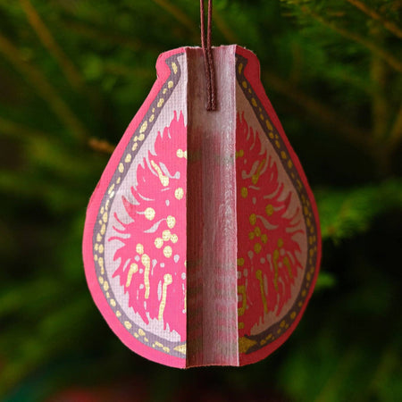 Decorative pink teardrop ornament with intricate patterns hanging against a green foliage background. | East End Press | Shop Fodder