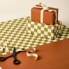 Two wrapped gifts with ribbons on a green and white checkered tablecloth, with scissors and additional ribbon. | Kinshipped | Shop Fodder