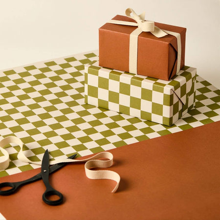 Two wrapped gifts with ribbons on a green and white checkered tablecloth, with scissors and additional ribbon. | Kinshipped | Shop Fodder