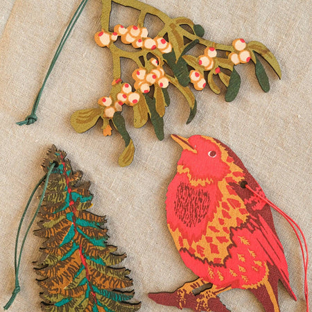 Decorative Christmas ornaments including a bird, tree, and mistletoe on a textured beige background.  | East End Press | Shop Fodder